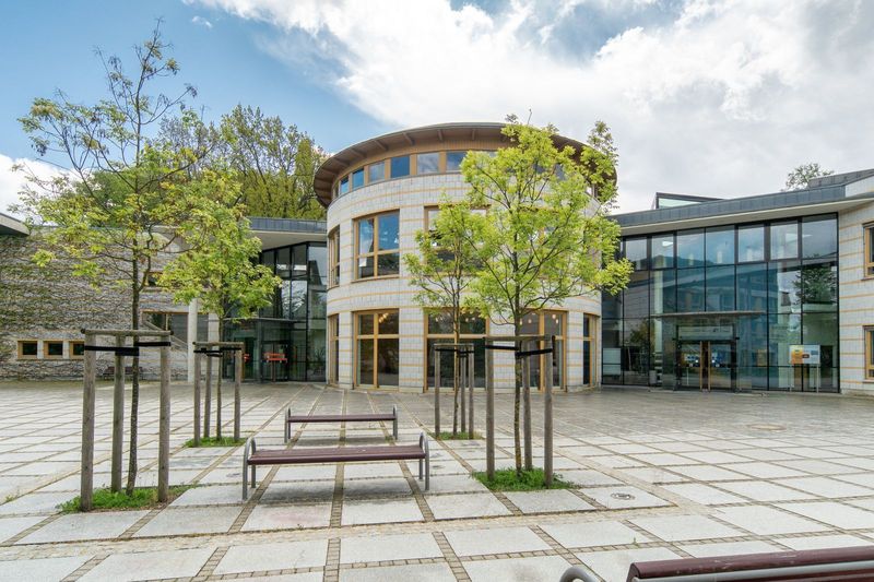 Moderner Gebäudekomplex mit gläsernem Rundbau und begrüntem Vorplatz