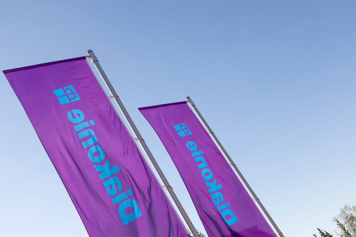Zwei violette Fahnen der Diakonie wehen vor blauem Himmel