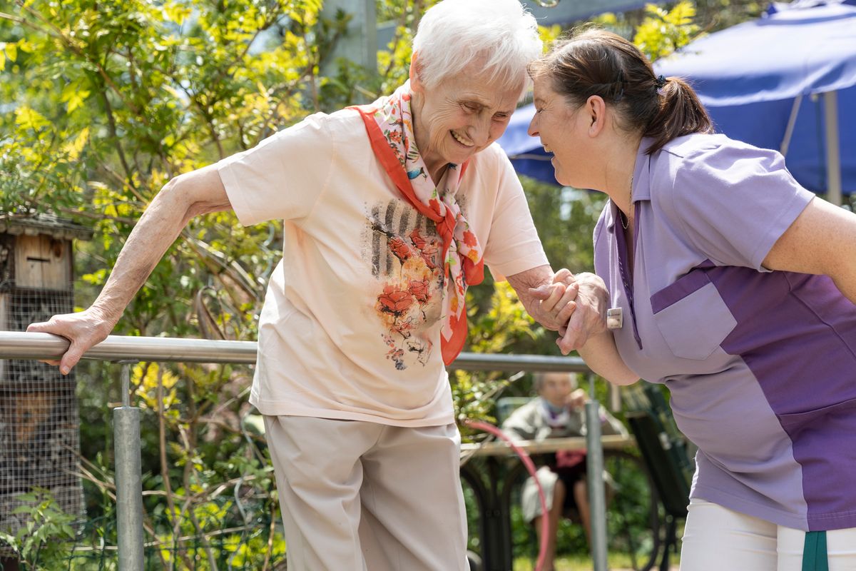 Pflegerin des Diakonischen Werks stützt eine ältere Dame beim Gehen im Garten