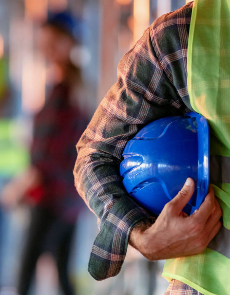 Bauarbeiter mit Warnweste trägt einen blauen Schutzhelm unter dem Arm