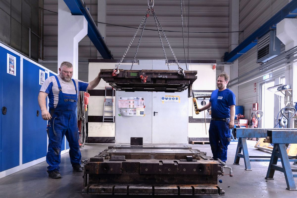 Zwei Mitarbeiter von Mitras Composites Systems verlagern mit einem Hallenkran ein schweres Presswerkzeug