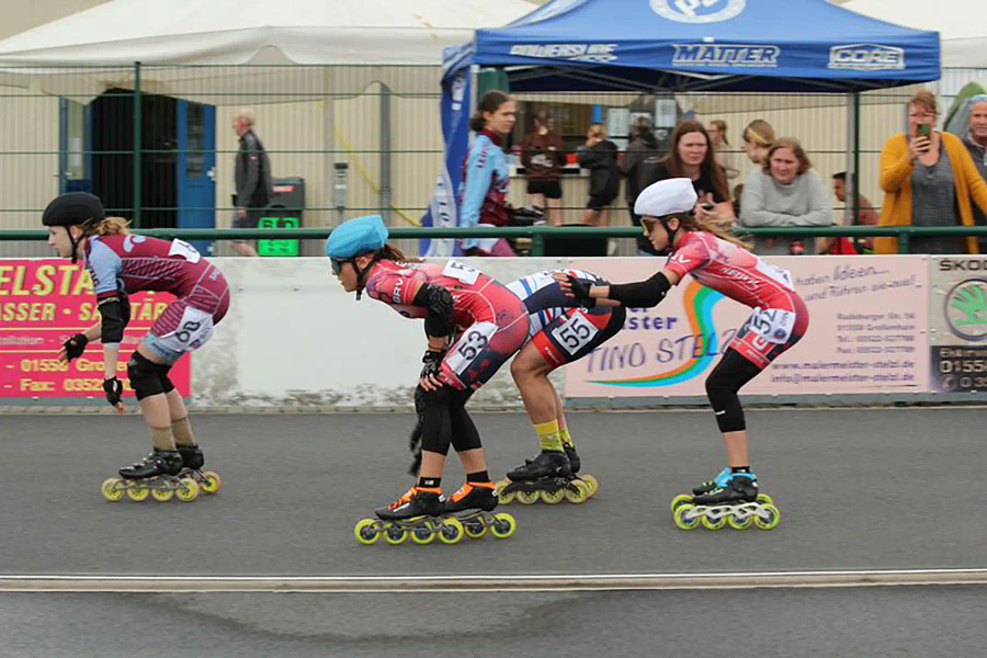 Drei Kinder in Rennanzügen beim Inline-Speedskating-Wettkampf