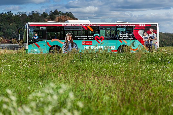 Linienbus mit MEISSNER-LAND-Werbung auf einer Landstraße, im Vordergrund eine Wiese