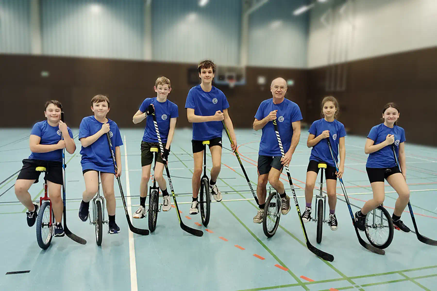 Einradhockey-Mannschaft mit Schlägern und Einrädern in einer Sporthalle