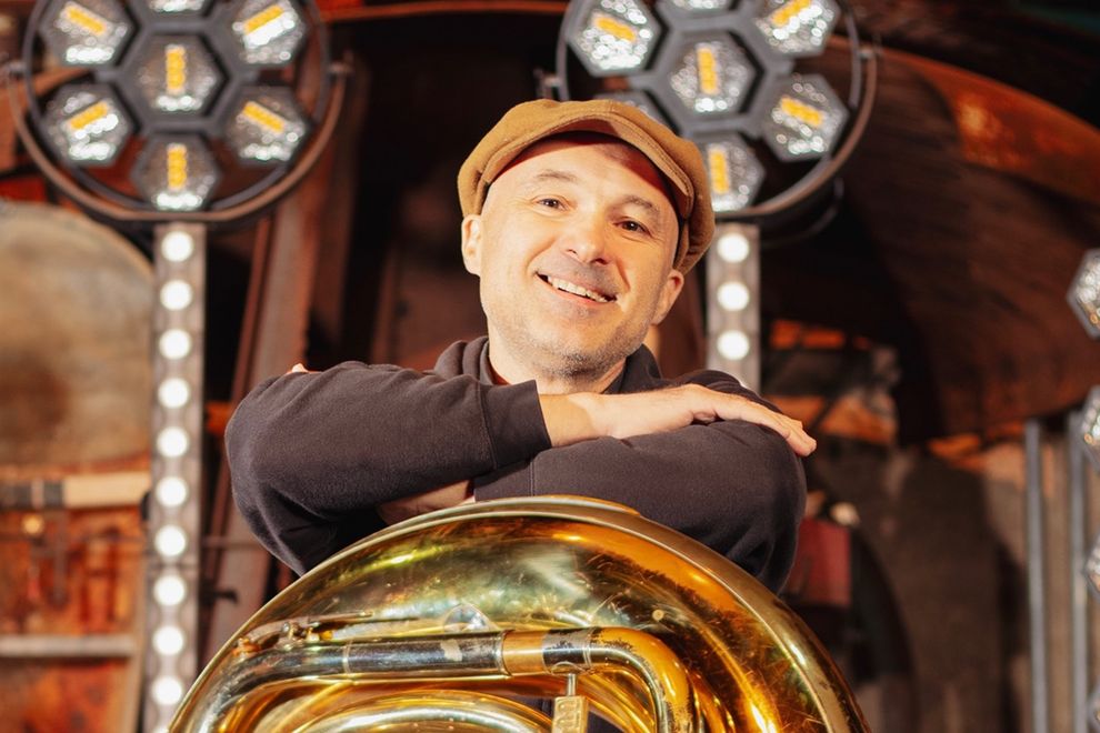 Musiker mit Schiebermütze lehnt lächelnd auf einer Tuba