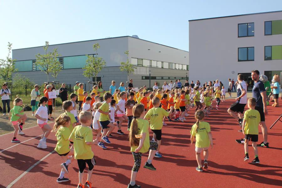 Viele Kinder in bunten Trikots laufen bei einem Sportfest auf einer Laufbahn